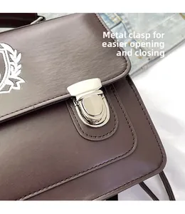 Detail showing the silver metal clasp and white embroidered logo on the brown messenger bag