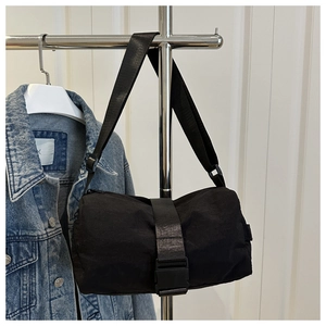 Detail of black cylinder oxford crossbody bag with adjustable buckle strap on denim jacket