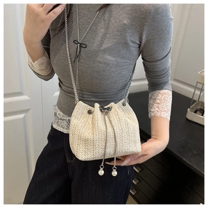 Detailed shot of straw woven bucket bag featuring drawstring pearls and silver chain strap