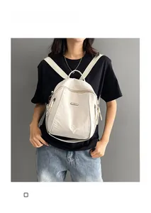 Detail of white nylon backpack with metal logo plate shown on model against gray wall
