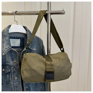 Olive green nylon crossbody bag with buckle detail hung near a denim jacket background