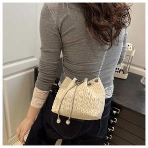 Detail of straw woven bucket bag with pearl drawstring and slim metal chain strap