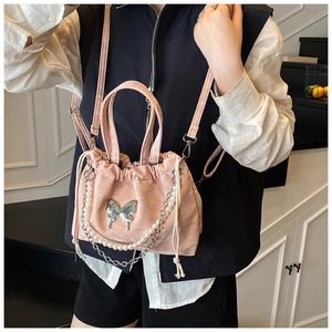 Detail of pink drawstring bucket bag featuring a silver butterfly charm and pearl chain
