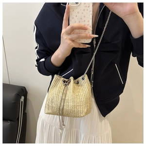 Detail of woven straw bucket bag featuring silver chain, metal bow and pearl charms