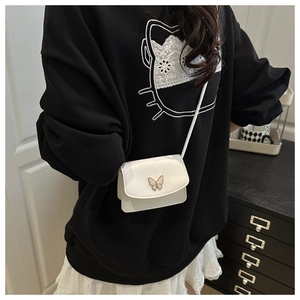 Detailed side view of white mini flap crossbody bag with metal butterfly buckle on a model