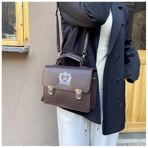 Détail du sac messager marron foncé vintage avec boucle argentée et logo écusson