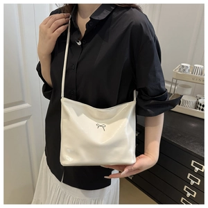 Detail of white patent leather shoulder bag with a metal bow accent on a model
