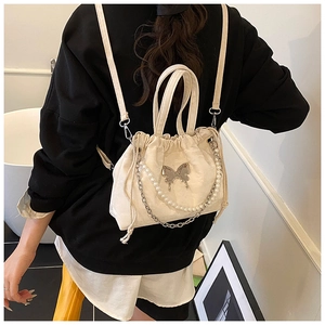 Detail of cream drawstring backpack featuring silver butterfly and pearl chain strap