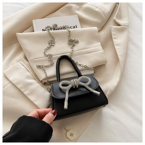Détail du mini sac en cuir noir mat avec un nœud en strass brillant et une chaîne argentée