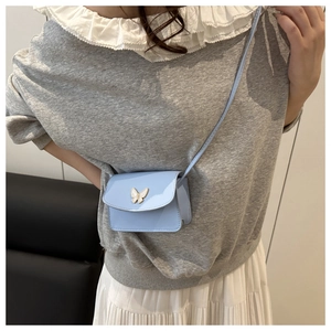 Detail of light blue patent leather mini bag with gold butterfly metal ornament