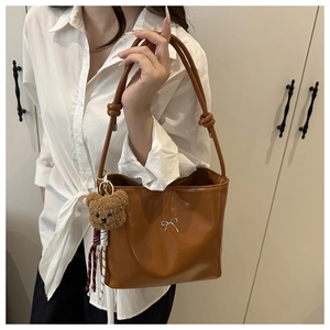 Detail of caramel hobo bag with silver bow accent and cute plush bear charm decoration