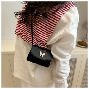 Detailed shot of a black mini crossbody bag with a white butterfly ornament on a white shirt