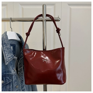 Detail of dark red glossy shoulder bag featuring silver metal bow and knotted strap