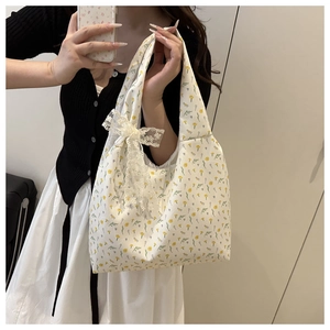 Detail of floral canvas tote bag featuring yellow flower patterns and a lace bow charm