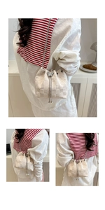 Detail of beige straw bucket bag featuring silver butterfly buckle and pearl drawstring