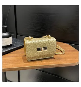 Detail view of gold woven texture small flap bag with a metal twist lock on a desk
