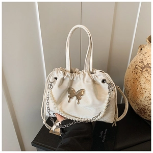 Close-up of pearl chain and silver butterfly charm on a cream pleated crossbody bag