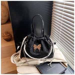 Detail of black drawstring handbag featuring golden butterfly badge and pearl chain