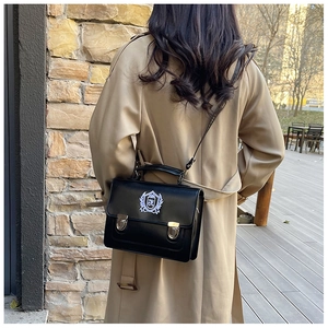 Vue de rue du sac messager en cuir noir avec écusson brodé et boucles métalliques