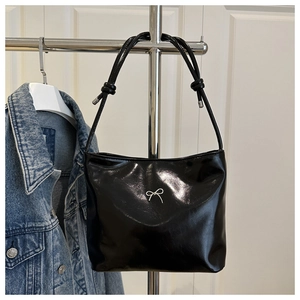 Close-up of black glossy bucket bag featuring a silver metal bow and knotted strap details