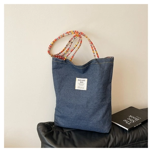 Detail of blue denim tote bag featuring colorful woven rope handles and red plaid lining