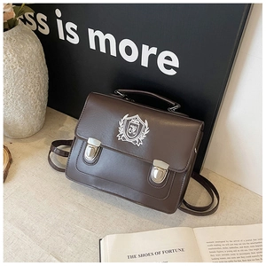 Détail du cartable en cuir marron foncé avec écusson brodé et fermoir métallique à poussoir