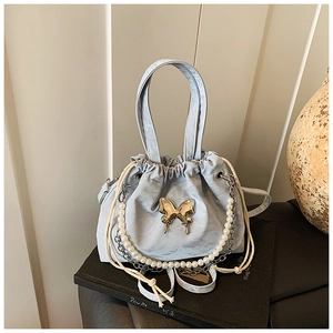 Close-up of light blue textured bucket bag with golden butterfly buckle and pearl chain