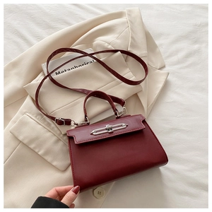 Detailed view of dark red textured leather handbag with silver metal lock on a beige blazer