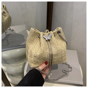 Detail of straw bucket bag featuring butterfly metal drawstring and pearl charm on chain