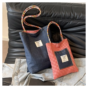 Detail of denim and plaid tote bags featuring colorful woven handles on a leather sofa