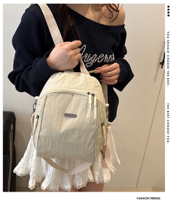 Detail of beige nylon backpack showing metal logo plate and pleated fabric texture