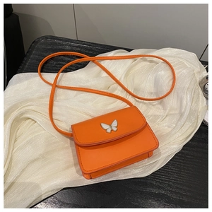 Detail shot of orange mini crossbody bag with a white butterfly buckle on silk background