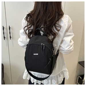 Dettaglio di un piccolo zaino in nylon nero con logo in metallo indossato dal modello