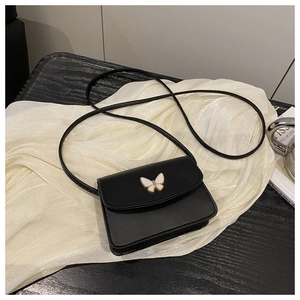 Detail of black crossbody bag with white butterfly metal ornament on a silk background