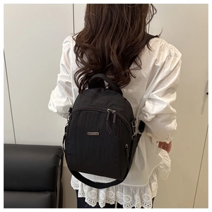Detail of a black nylon backpack featuring a silver metal logo and zipper pocket