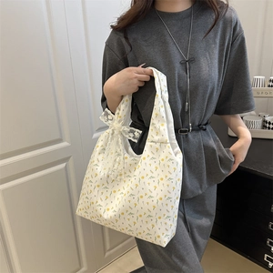 Floral canvas shoulder bag with white lace bow detail worn by a model in casual grey suit