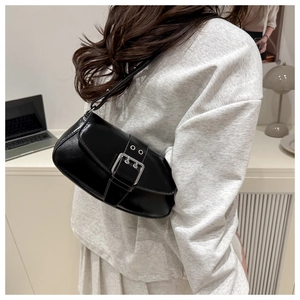 Detail of black glossy leather underarm bag with silver buckle worn by a model