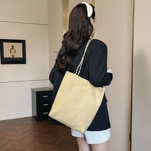 Sac cabas en toile beige avec bandoulière en perles porté par un mannequin élégant