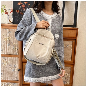 Close-up of lightweight cream nylon backpack with silver metal logo and zip pockets