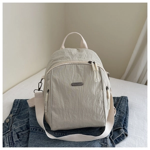 Detail of beige nylon backpack with pleated texture and metal logo on denim fabric
