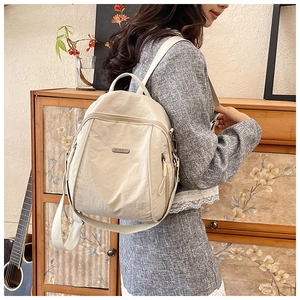 Detail of beige nylon backpack with adjustable straps and metal logo in home setting