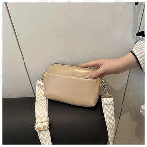 Détail d'un sac bandoulière beige avec large sangle géométrique et boucles dorées