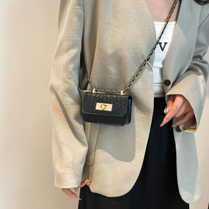 Mini black quilted shoulder bag with gold chain strap and turn-lock closure on model