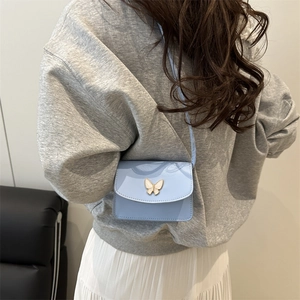 Women's light blue crossbody bag with butterfly buckle on model with skirt