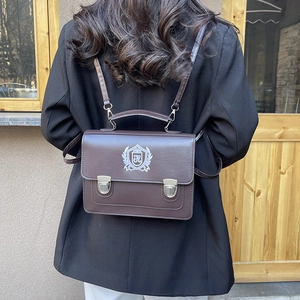 Sacoche rétro marron style collège avec écusson brodé blanc porté comme un sac à dos