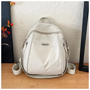 Detail view of cream nylon backpack featuring metal brand plate and side zipper pockets