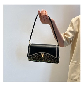 Detail of black underarm bag with white stitching, gold clasp, and colorful sequins