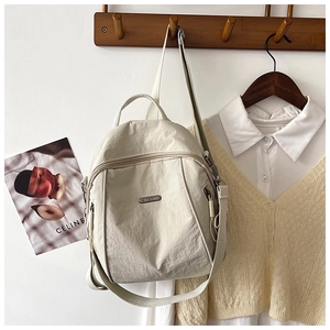 Detail of light beige nylon backpack with metal brand logo and premium texture hanging on hook