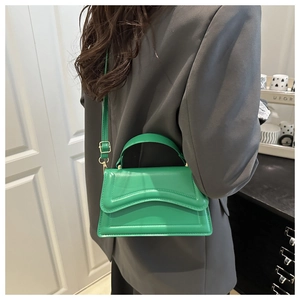 Model styling a vibrant green crossbody bag with unique wavy edges and gold hardware