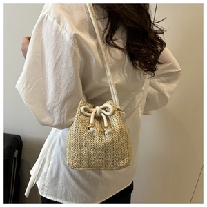 Detail of a beige woven bucket bag with drawstring closure and golden bead accents